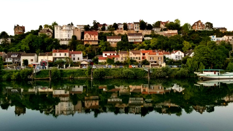 View from a river cruise of homes along the banks of the Seine reflected in the water