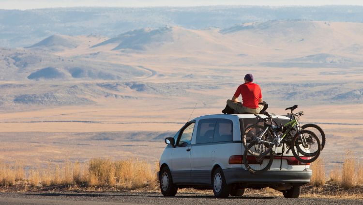 Man taking a break on a road trip, sitting on top of his car