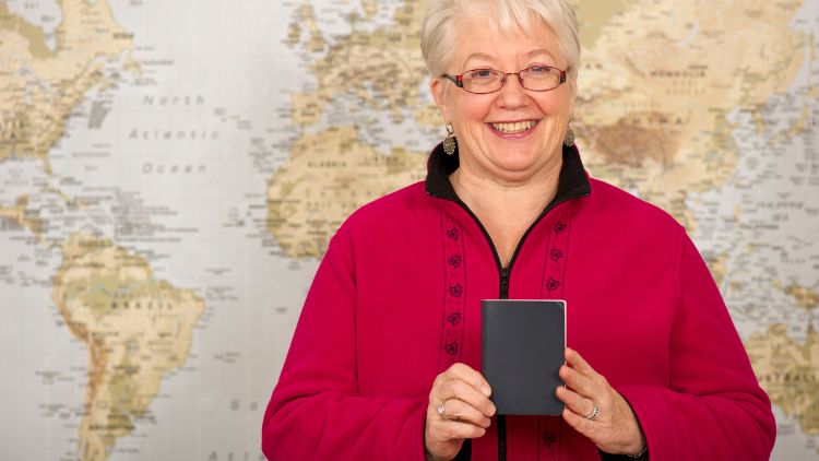 senior woman standing in front of a map holding a passport, preparing for first time solo travel