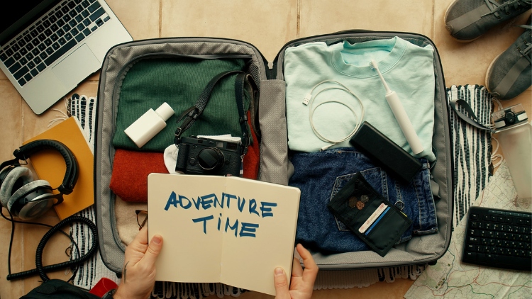 open suitcase and hands holding notebook that says: adventure time