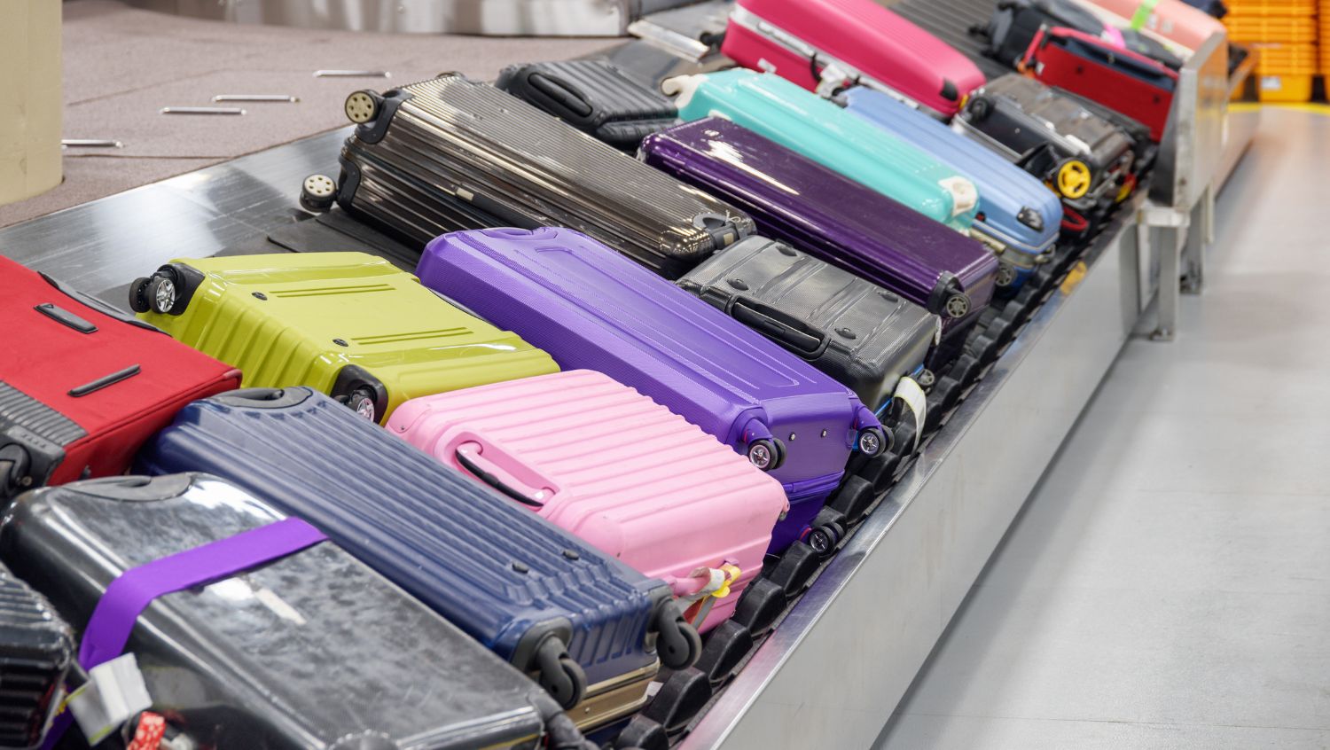 One of the best checked baggage tips is illustrated in this image of multicolored suitcases on a luggage carousel.