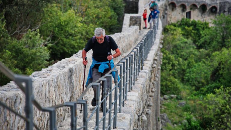 man crossing bridge using walking poles