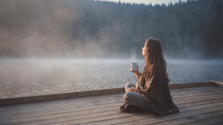 woman sitting on dock holding coffee