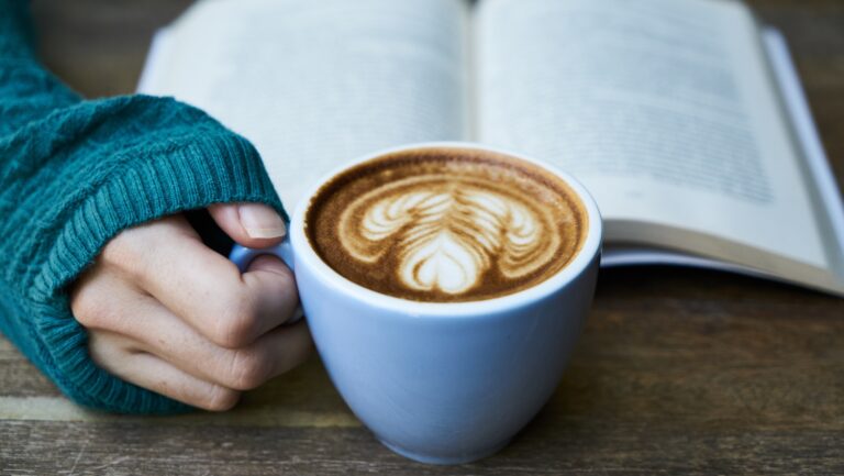 hand holding mug of coffee and open book